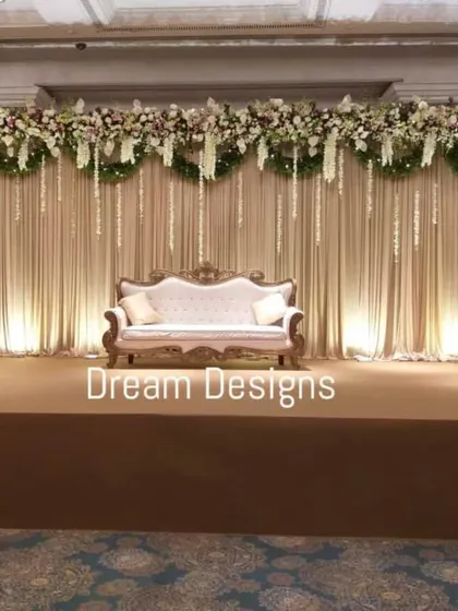 A classic and elegant stage design for a formal reception. The backdrop features soft, pleated draping with a heavy floral border and delicate hanging elements, creating a sophisticated and timeless look.