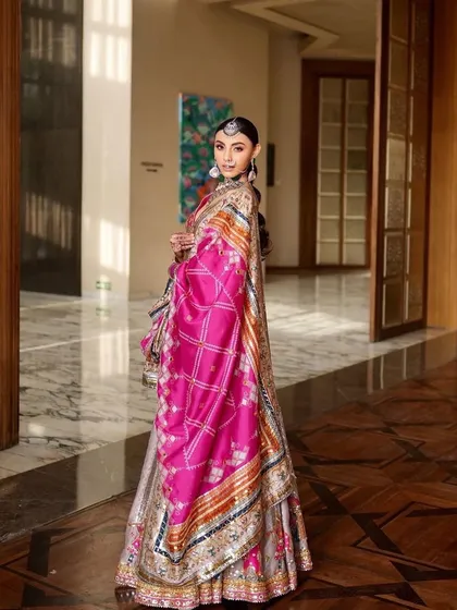 A full-length view of a vibrant Punjabi bridal look. The bright pink dupatta and intricate lehenga are balanced with fresh, glowing makeup that is perfect for a day wedding.