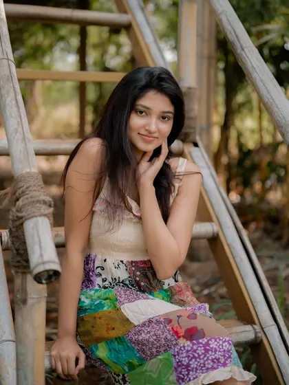 A candid and happy portrait of actress Rachana Inder on a bamboo ladder. The natural, outdoor setting and her bright smile create a joyful and authentic image.