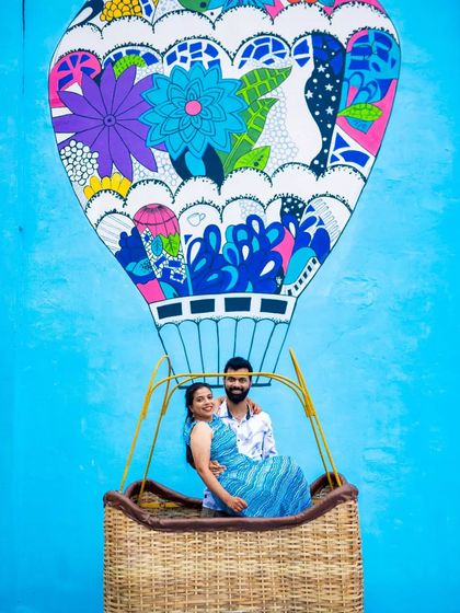 A playful and creative shot of a couple sitting in a basket in front of a colorful hot air balloon mural. We use vibrant urban art to make your couple portraits pop.
