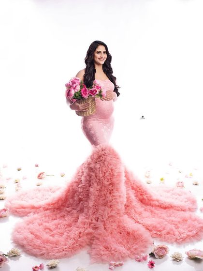 A stunning portrait of a mom-to-be in a pink ruffled mermaid gown, surrounded by scattered rose petals. The high-key lighting creates a bright and joyful atmosphere.