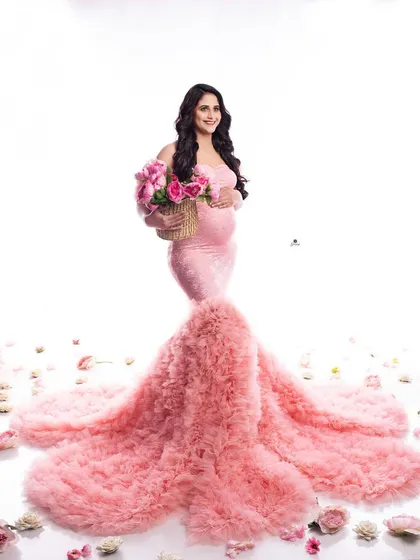 A stunning portrait of a mom-to-be in a pink ruffled mermaid gown, surrounded by scattered rose petals. The high-key lighting creates a bright and joyful atmosphere.