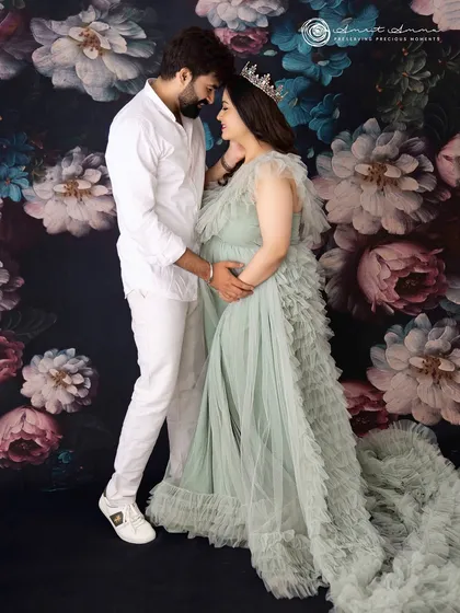 An intimate and tender moment. The simple white outfits contrast beautifully with the dark floral backdrop, drawing all attention to the couple's loving connection.