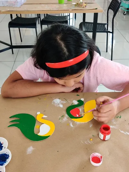 A young girl painting peacock-shaped T-light holders, a popular craft during our Diwali workshops.