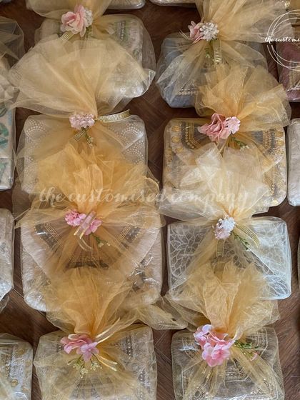 Beautifully wrapped mehendi favors for your special occasion. These gifts are elegantly packaged in gold net and adorned with small pink flowers, ready to delight your guests.