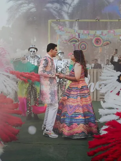 The couple's grand entry at their carnival-themed event, surrounded by dancers in elaborate costumes and a cloud of smoke, creating a dramatic and festive moment.