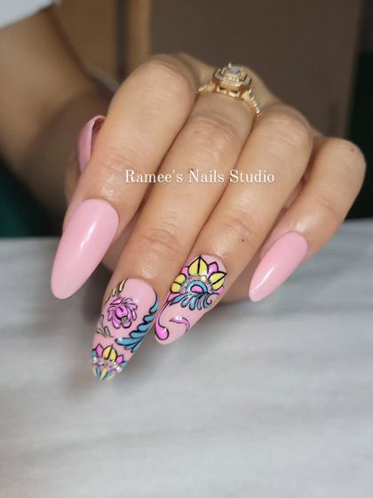 Intricate hand-painted nail art for Navratri. This design uses a soft pink base and features colorful, detailed patterns inspired by traditional Indian art.