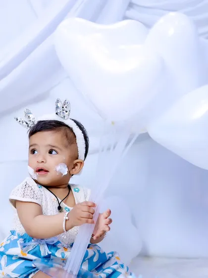 A sweet moment from the all-white birthday shoot, with the baby girl holding heart-shaped balloons.