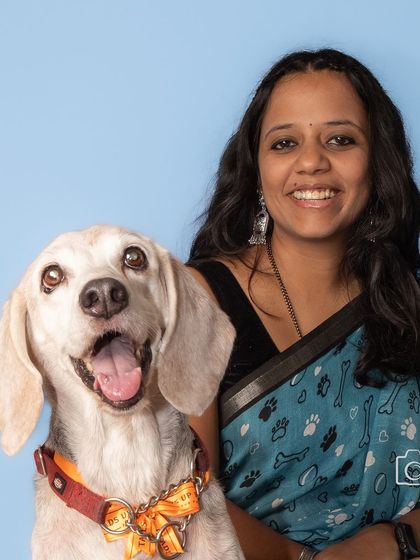 A classic, smiling portrait of Kavitha and her handsome beagle, Seenu, against a bright blue background. A timeless memory of their special bond.