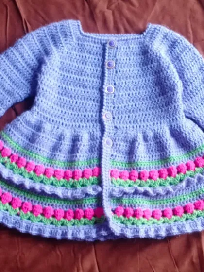 This lavender baby frock features beautiful bobble stitch detailing on the skirt for a lovely texture. The mix of pink and green stripes adds a playful touch of color.