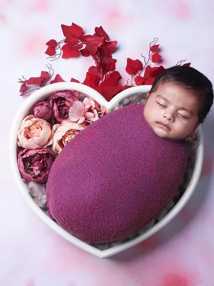 A baby wrapped in a rich magenta swaddle, sleeping in a heart-shaped bowl filled with pink and red flowers. This is a popular choice for a floral-themed newborn shoot.