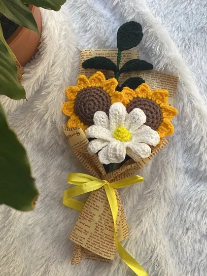 A cheerful bouquet of two crochet sunflowers and a white daisy. The newspaper wrapping and yellow ribbon give it a sunny, rustic feel.