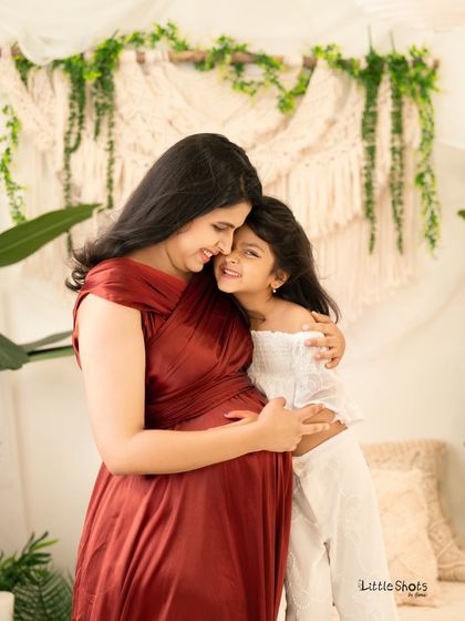 A heartfelt hug between a mother and her daughter, both excited for the new baby. This maternity photo captures the sweet bond they share in a bright, nature-inspired studio setting.