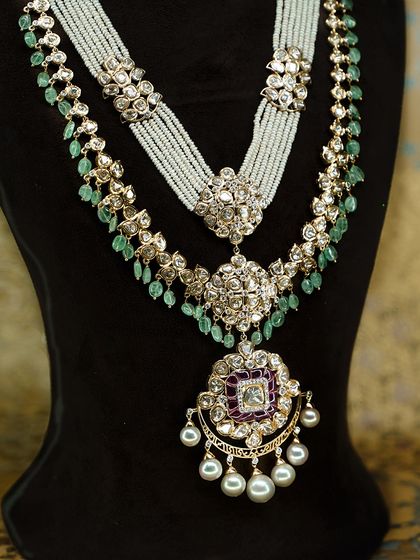 A layered polki and pearl necklace designed for a royal bridal look. This piece features emerald drops and a stunning pendant with a central ruby accent, creating a feeling of pure grandeur.