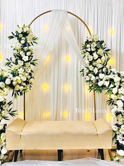A clean and modern Roka setup using a golden C-shaped arch frame. The asymmetrical white floral arrangements add a contemporary touch against the fairy-lit backdrop.