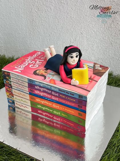For a girl who loves to read, we created this cake designed to look like a stack of Enid Blyton's "Naughtiest Girl" books, complete with a fondant figurine of her reading on top.