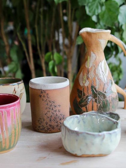 A beautiful collection of hand carved and painted pieces, including a large pitcher with lily motifs and mugs with intricate patterns.