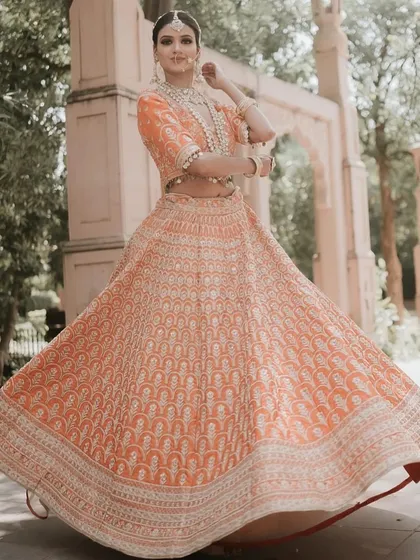 A peach-colored lehenga with intricate white embroidery, shot against a heritage backdrop. The full-length and twirling shots show its grace and elegance.