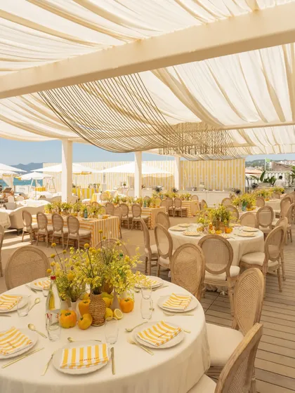 The dining setup for the Cannes Mehendi featured round tables with yellow and white striped linens, rattan chairs, and fresh yellow floral centerpieces, creating a cheerful, summery vibe.