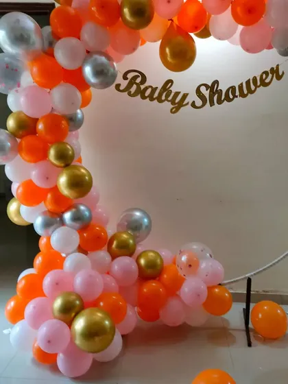 A simple and elegant baby shower balloon arch for a home celebration, using pink, orange, and gold balloons.