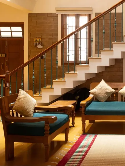 The living area seating arrangement, with simple wooden furniture against a backdrop of exposed brick and a gracefully ascending staircase.