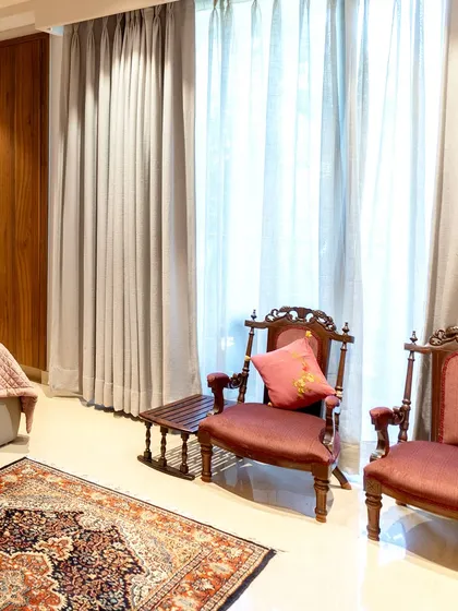 We believe in creating intimate nooks within larger spaces. This seating area features vintage-style carved chairs with plush upholstery, set against floor-to-ceiling curtains that filter natural light beautifully.