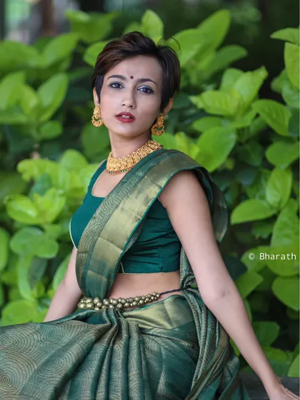 This outdoor portrait blends traditional and modern styles. The vibrant green of the silk saree stands out against the natural foliage, and the model's contemporary pixie cut adds a unique, edgy twist to the ethnic look.