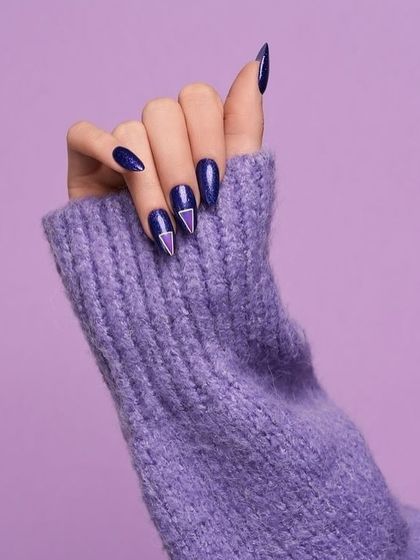 A close-up of a hand with a deep purple manicure against a matching sweater. The textural contrast and monochrome color scheme create a cozy and chic image.