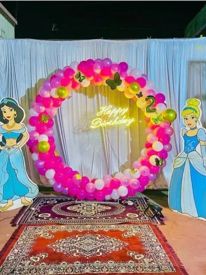 A royal celebration with a Disney Princess theme. This circular balloon arch in pink and yellow is flanked by life-sized cutouts of Princess Jasmine and Cinderella, perfect for a magical birthday.