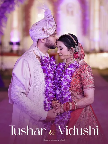 An intimate portrait of the groom kissing his bride's forehead, their purple garlands adding a pop of color.