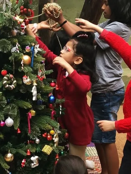 Children of all ages come together to decorate the Christmas tree. Each child adds an ornament, contributing to a beautiful, shared creation that marks the festive season.