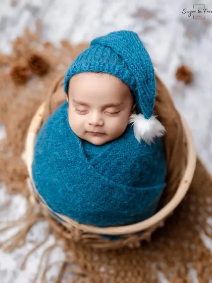 An adorable newborn boy, snugly wrapped in a blue swaddle and wearing a matching sleepy cap, resting peacefully in a rustic basket.
