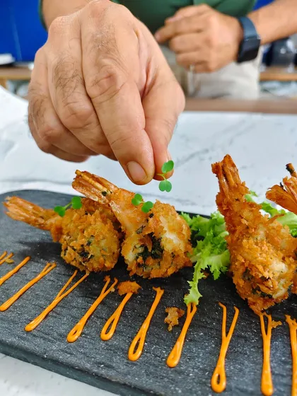 Precision meets passion. Here, our chef adds a delicate microgreen, the final touch to our Panko Crumb Chimichurri Prawns, ensuring every plate is a work of art.