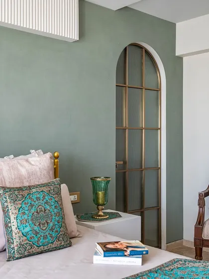 The master bedroom from the 'Eternity' project, featuring a serene sage green accent wall and a beautiful arched doorway with a fluted glass panel. The turquoise patterned cushions add a pop of color.