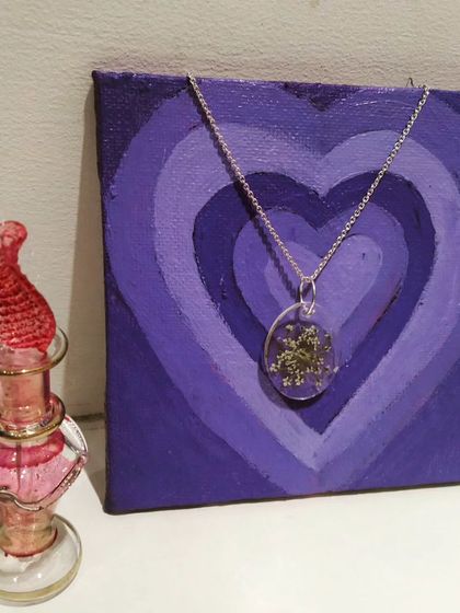 An oval-shaped resin necklace filled with delicate, wispy white flowers. This piece has a timeless, classic feel and is perfect for everyday wear.