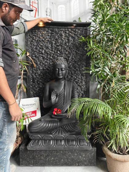 An artisan adjusts the top light on the black marble Buddha fountain, demonstrating the scale and hands-on quality check each piece receives.