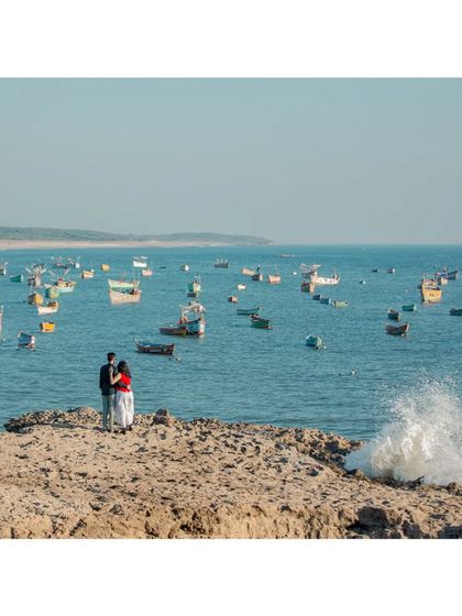 A stunning wide-angle shot of a couple standing on a rocky outcrop, surrounded by a sea full of colourful fishing boats.