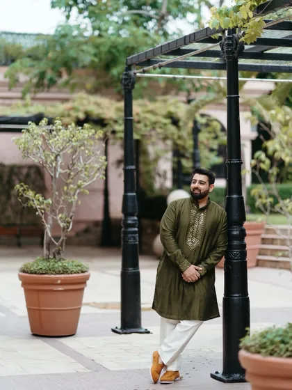 A relaxed portrait of the groom during the mehndi ceremony. Leaning against a post in a garden setting, he exudes a cool and casual confidence.