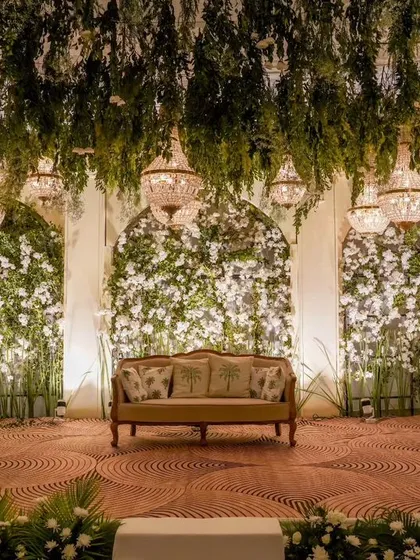 The stage is the heart of any reception. I designed this one with a ceiling of hanging greenery and crystal chandeliers above walls of white flowers, creating a lush, romantic backdrop for the couple.