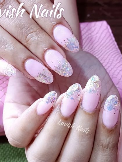 A glitter fade using iridescent flakes over a soft pink acrylic base on almond-shaped nails.