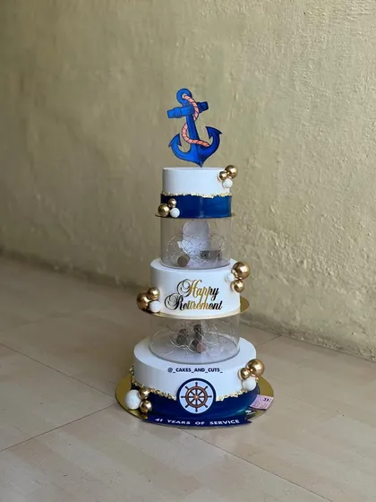 We were honored to create this special five-tier retirement cake for a Navy officer. The design incorporates a nautical theme with an anchor topper, a ship's wheel, and clear acrylic tiers filled with fairy lights for a beautiful glow.