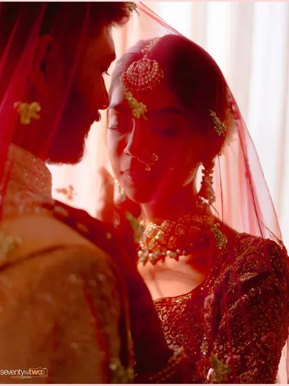 An intimate close-up of the couple, their faces close, captured through the bride's sheer red veil. A moment of quiet connection and love.