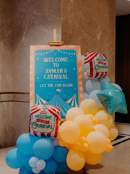 A "Welcome to the Carnival" sign at the party entrance. The sign is flanked by colorful balloon arrangements and themed foil balloons, setting a festive mood from the start.