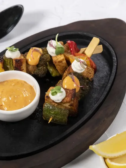 Grilled vegetable skewers served on a hot plate with a side of flavourful dipping sauce. A healthy and delicious vegetarian tapa option.