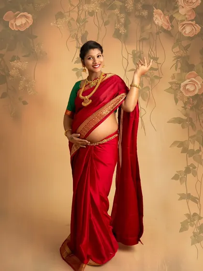 A stunning portrait of a mother-to-be in a vibrant red saree, showcasing her baby bump. The pose is confident and graceful, celebrating the beauty of her changing body.
