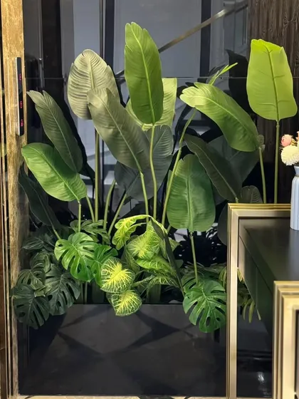 A lush arrangement of artificial tropical plants, including Bird of Paradise and Monstera, fills an awkward niche. This zero-maintenance solution brings vibrant, year-round greenery to a modern interior.