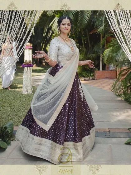 A bride looking ethereal in a purple Banarasi silk lehenga with polka dots. Her custom off-white blouse and sheer dupatta create a look of timeless grace.