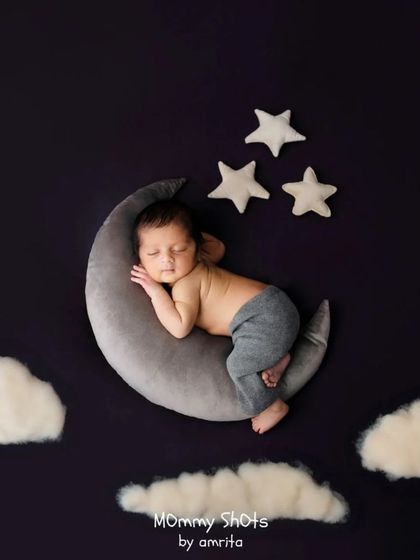 A dreamy portrait of a newborn on a moon prop against a dark, starry background.