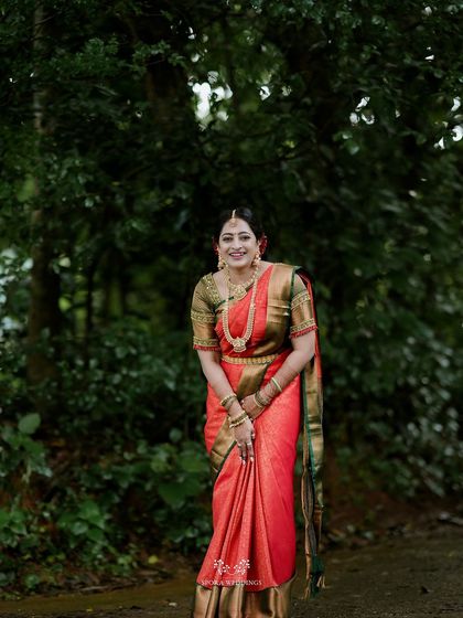 A portrait of the bride standing in a green, wooded area, her red saree a vibrant splash of color.