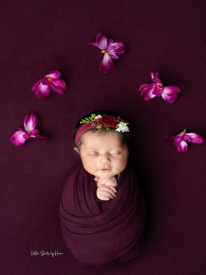 A top-down view of this beautiful plum-themed setup, showing the baby perfectly swaddled and surrounded by delicate flower petals.